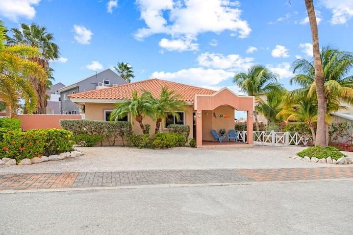 A classic Curaçao bungalow-style house with terracotta roof and palm trees